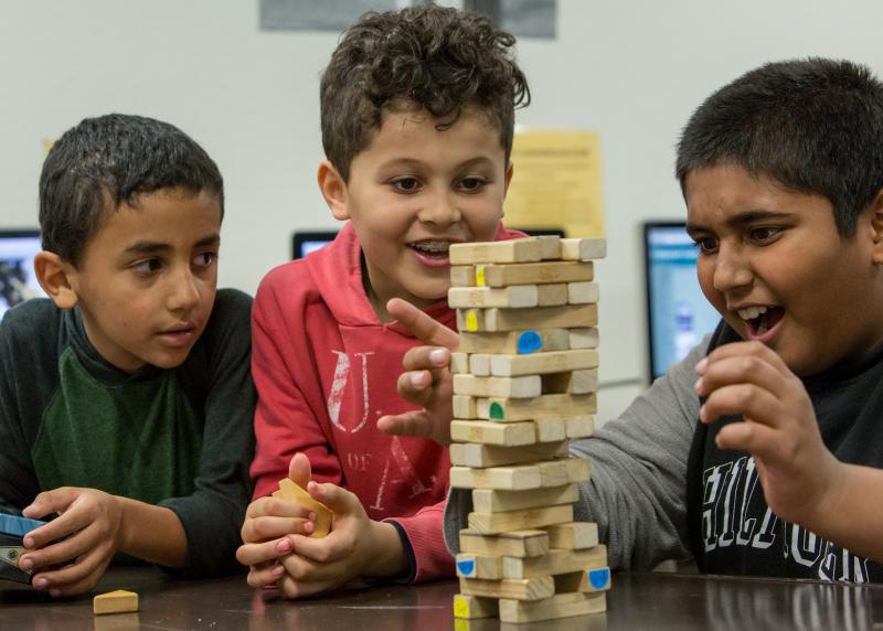 A multi-racial group of young boys excitedly play jenga 