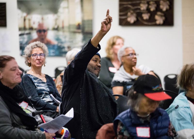 A black man raises his hand at a community meeting